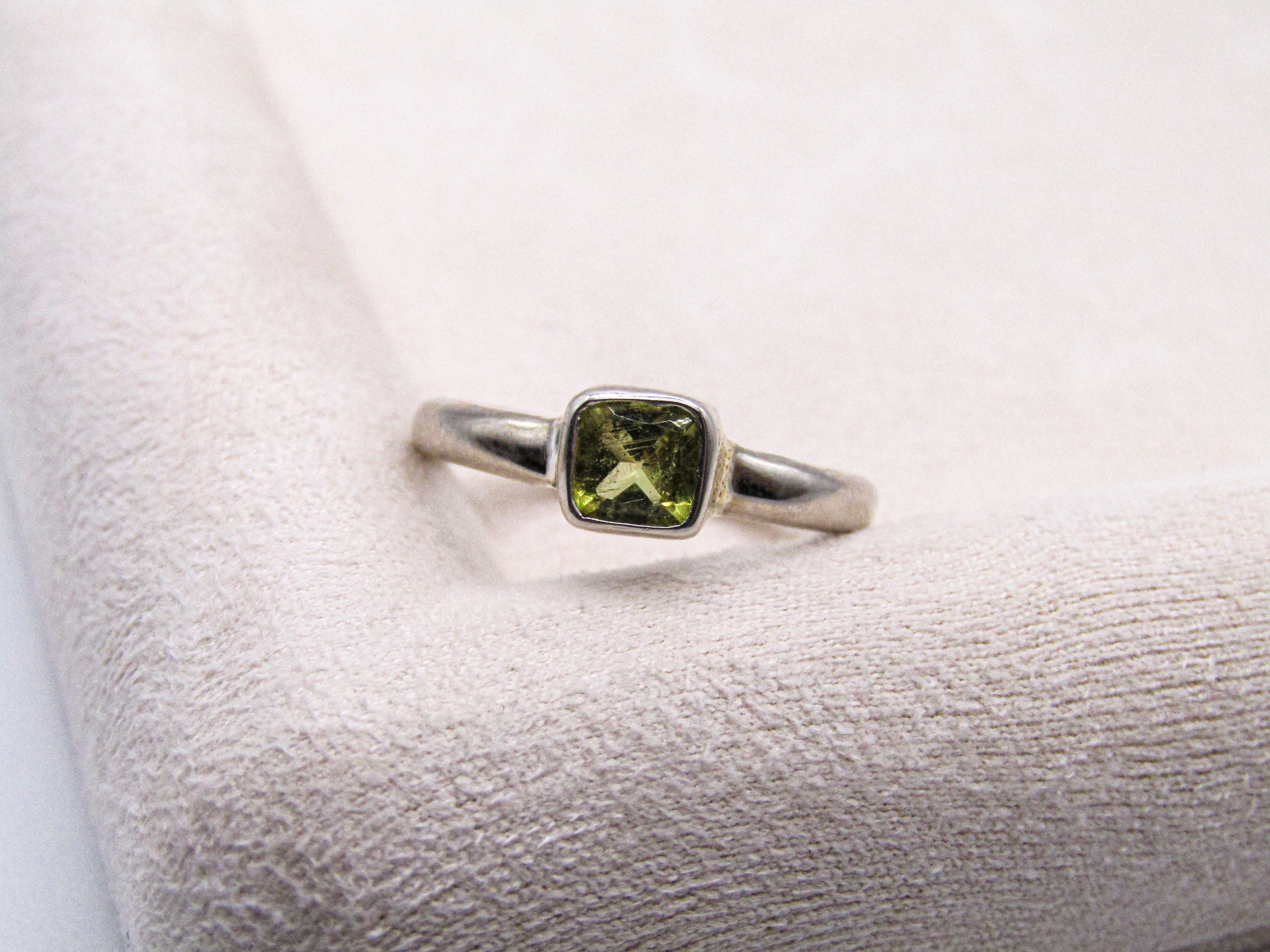 Silver ring with a green gemstone on a textured white surface