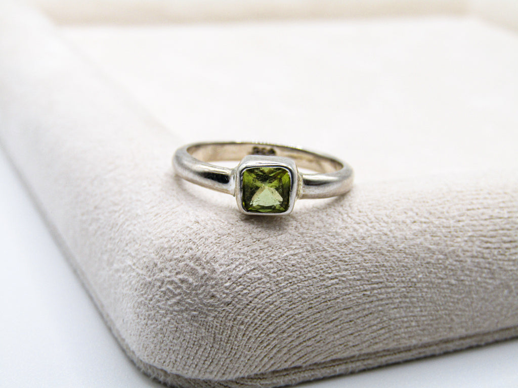 Silver ring with a green gemstone on a textured white surface