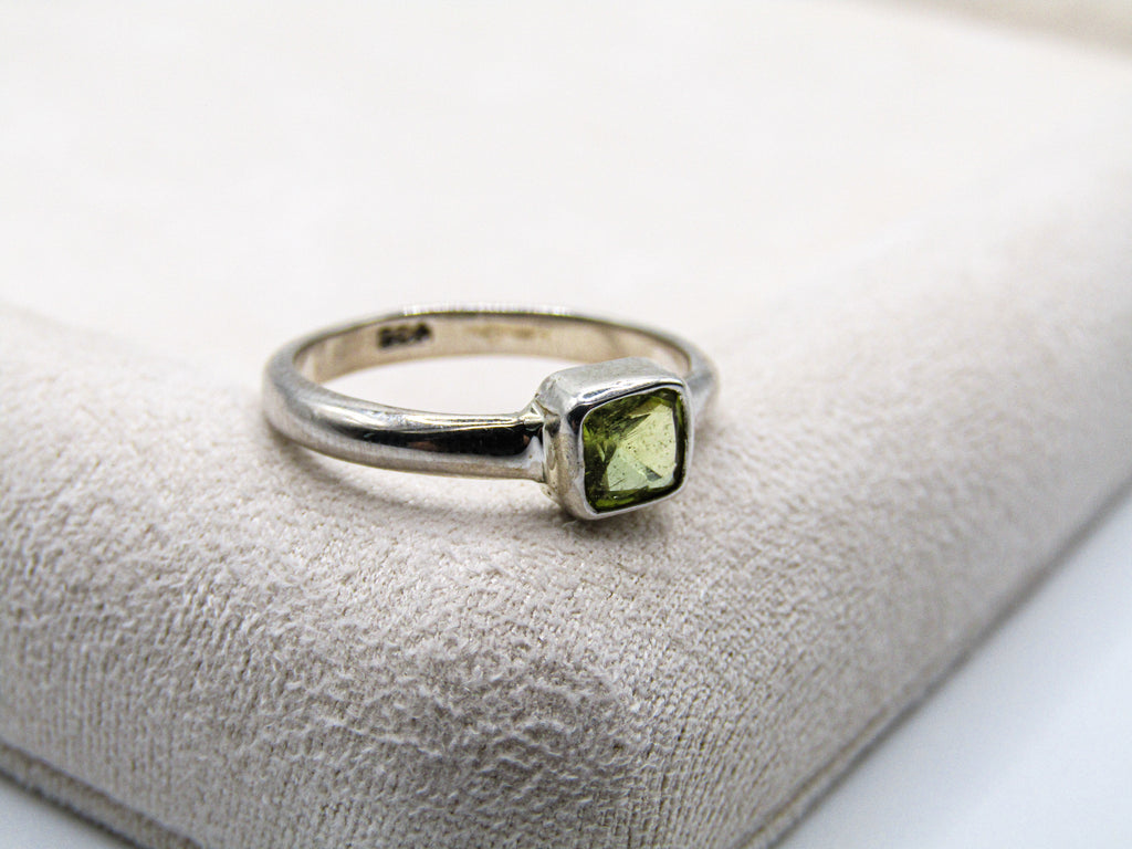 Silver ring with a green gemstone on a textured white surface