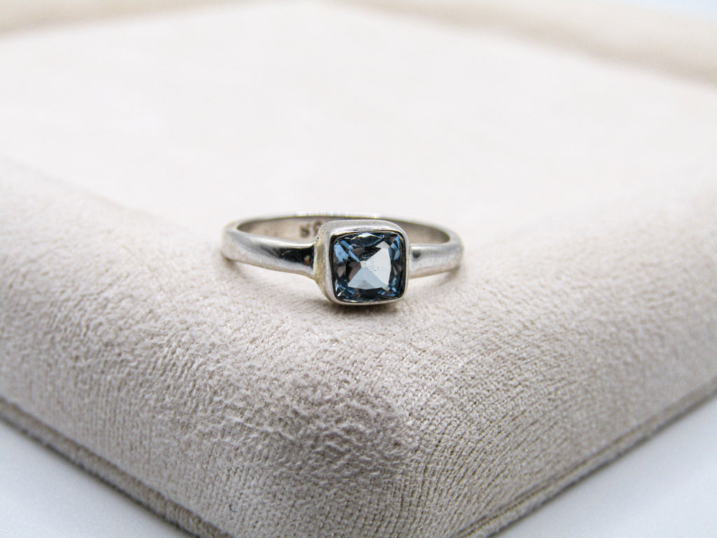 Silver ring with a blue gemstone on a textured beige surface