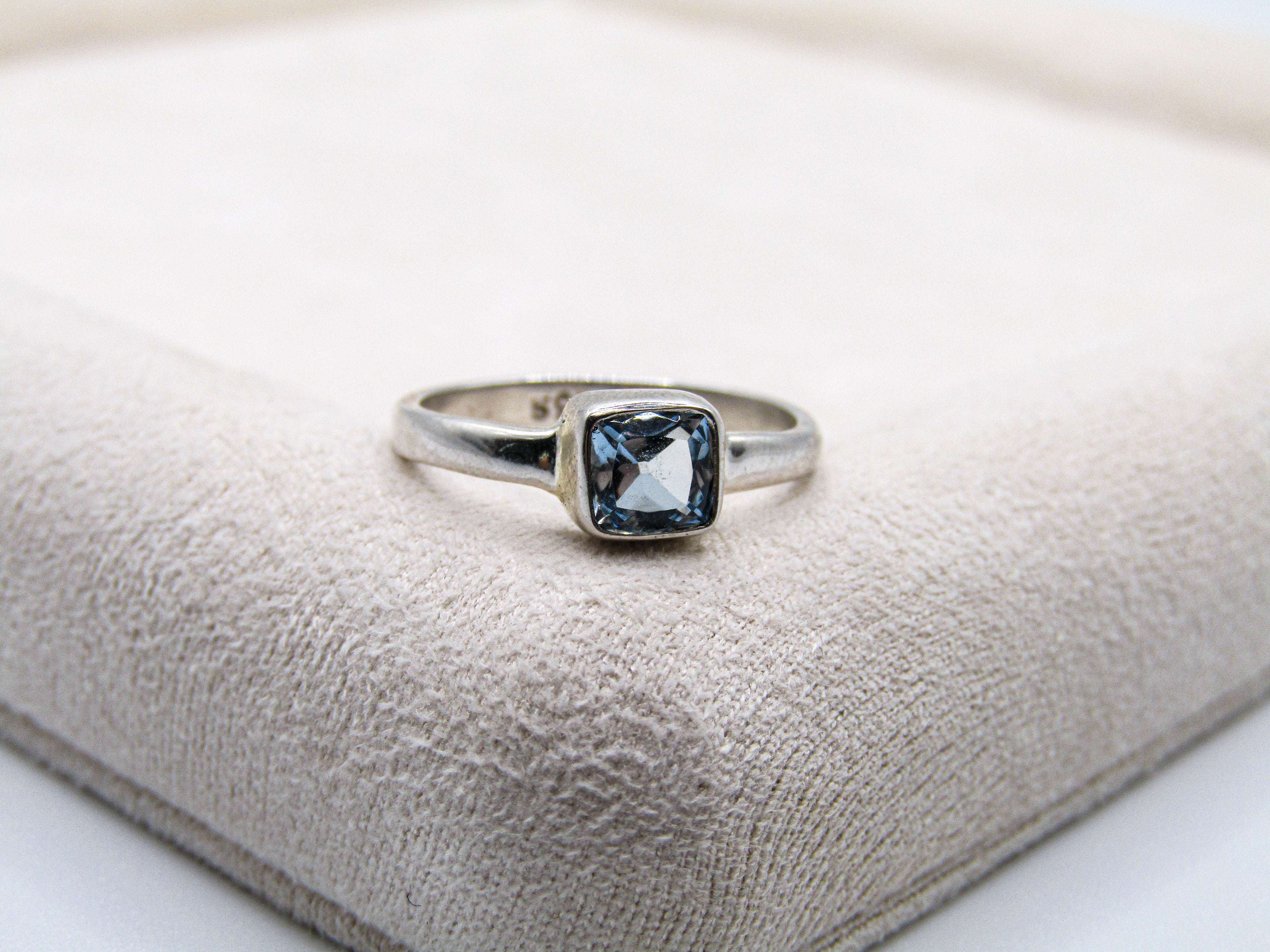 Silver ring with a blue gemstone on a textured beige surface