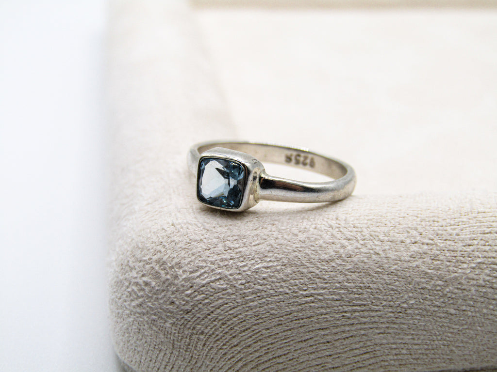 Silver ring with a blue gemstone on a textured white surface