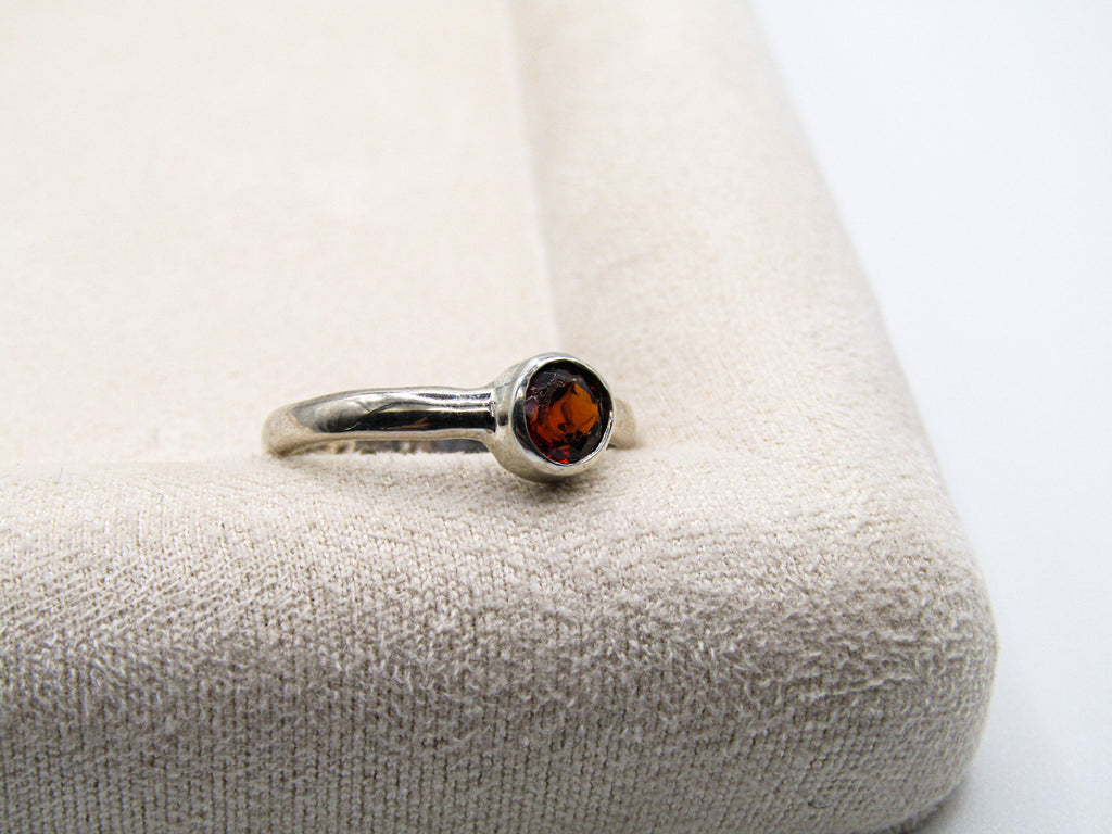 Silver ring with a red gemstone on a textured beige surface