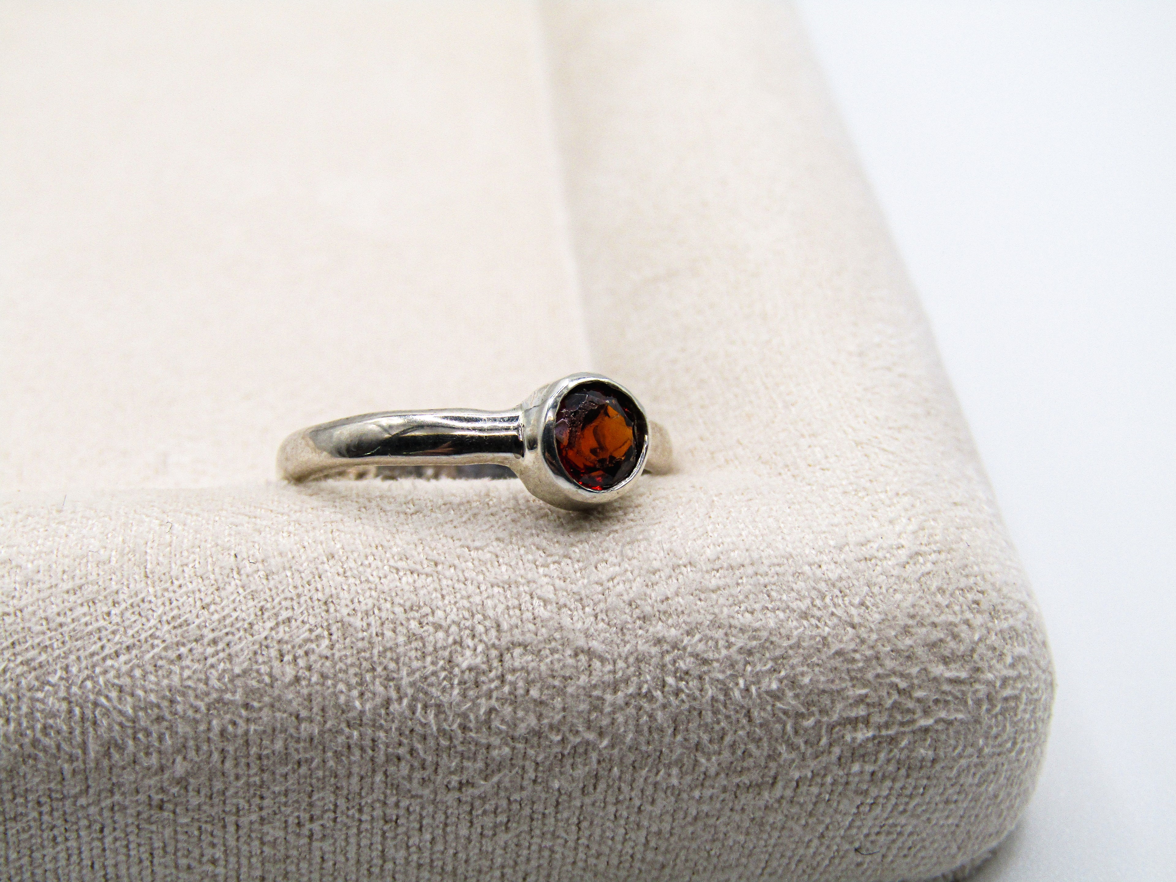 Silver ring with a red gemstone on a textured beige surface