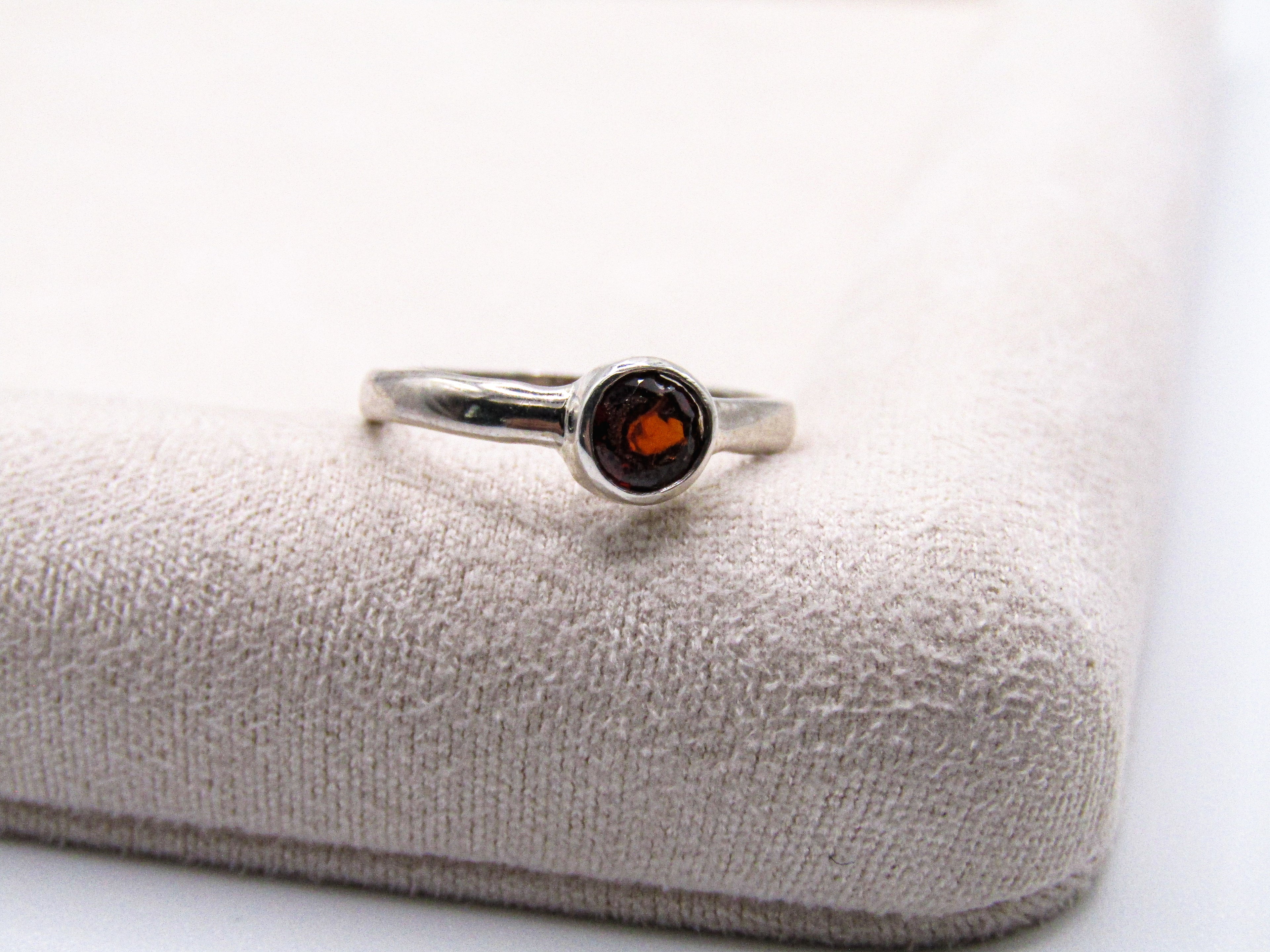 Silver ring with a red gemstone on a textured white surface