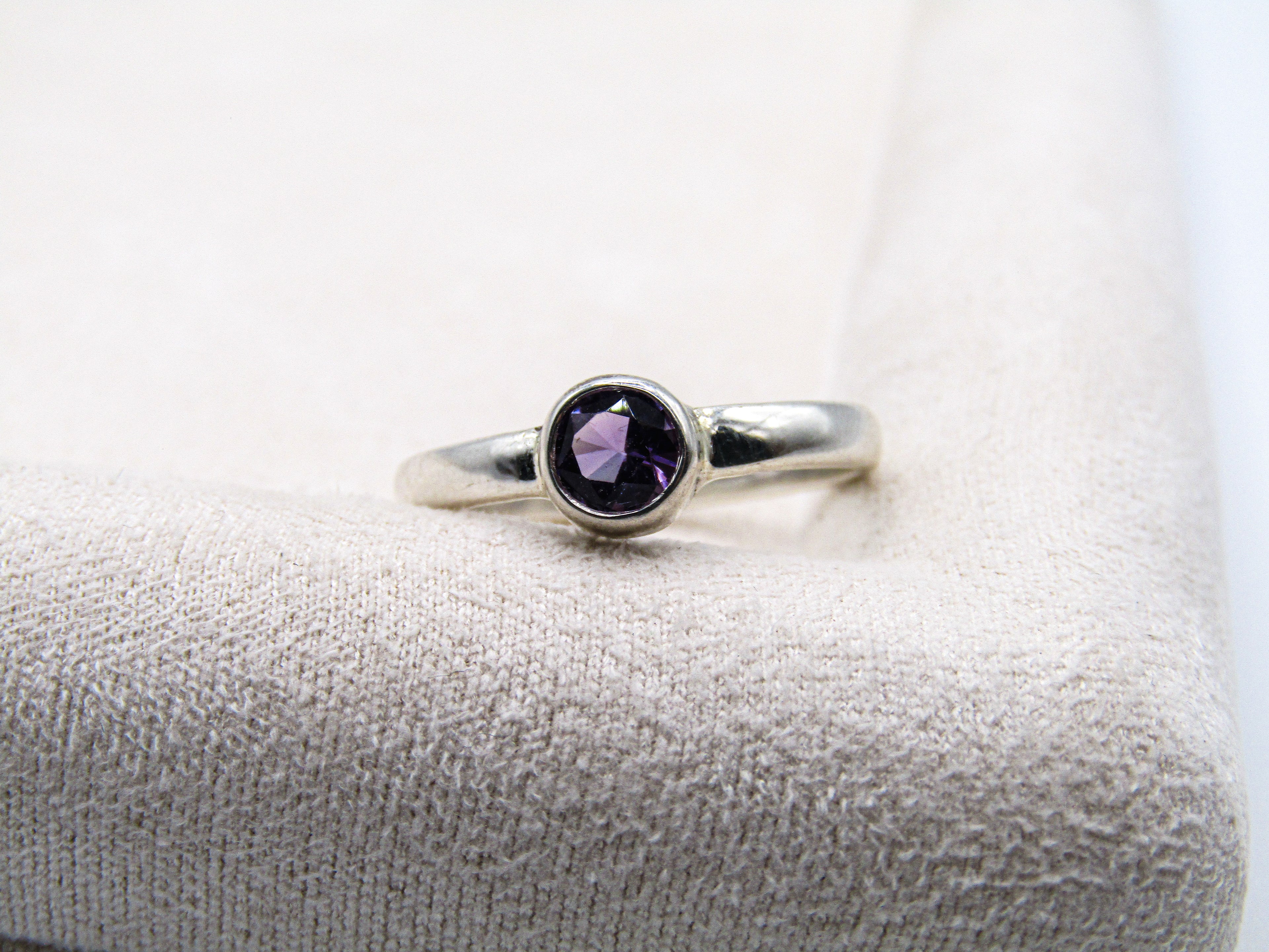 Silver ring with a purple gemstone on a white cushion