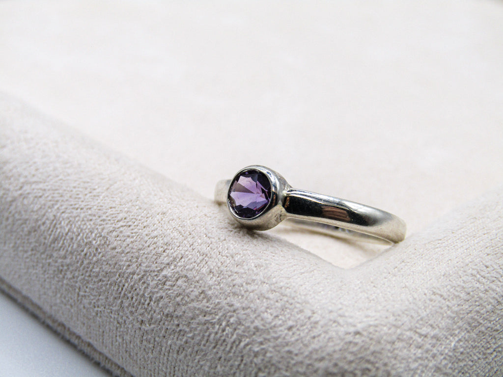 Silver ring with a purple gemstone on a white cushion