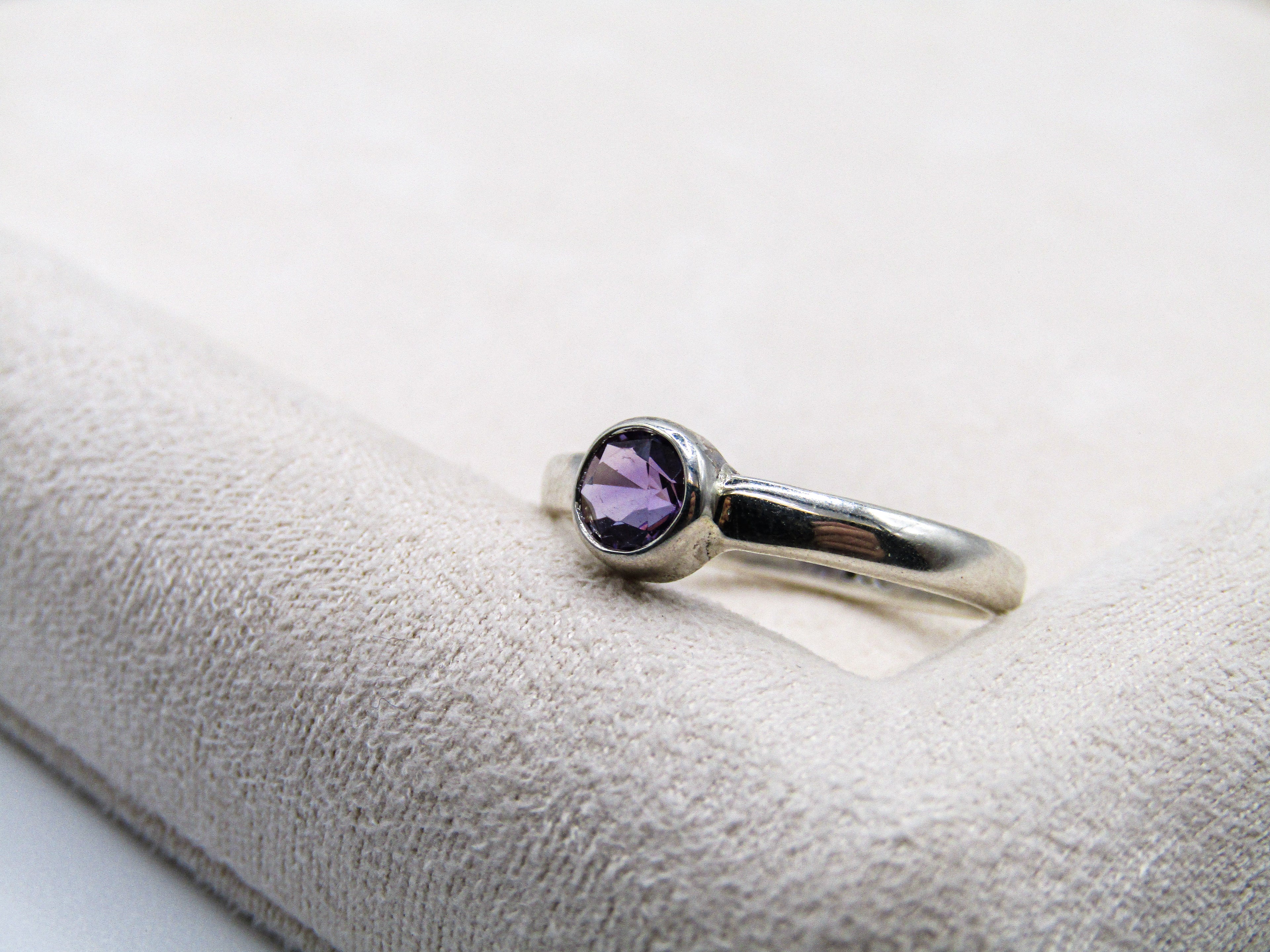 Silver ring with a purple gemstone on a white cushion