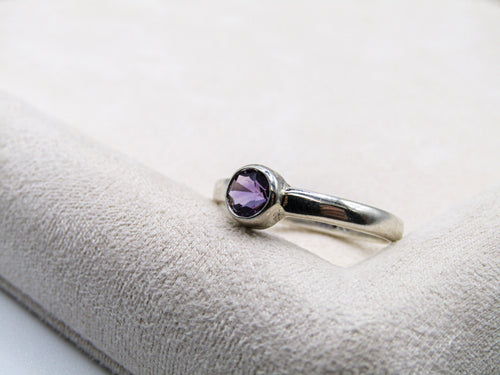 Silver ring with a purple gemstone on a white cushion