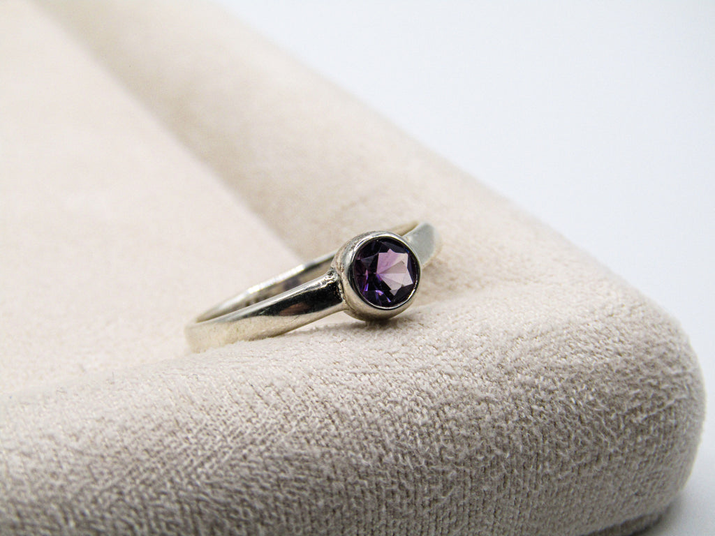 Silver ring with a purple gemstone on a textured white surface