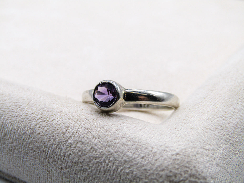 Silver ring with a purple gemstone on a textured white surface