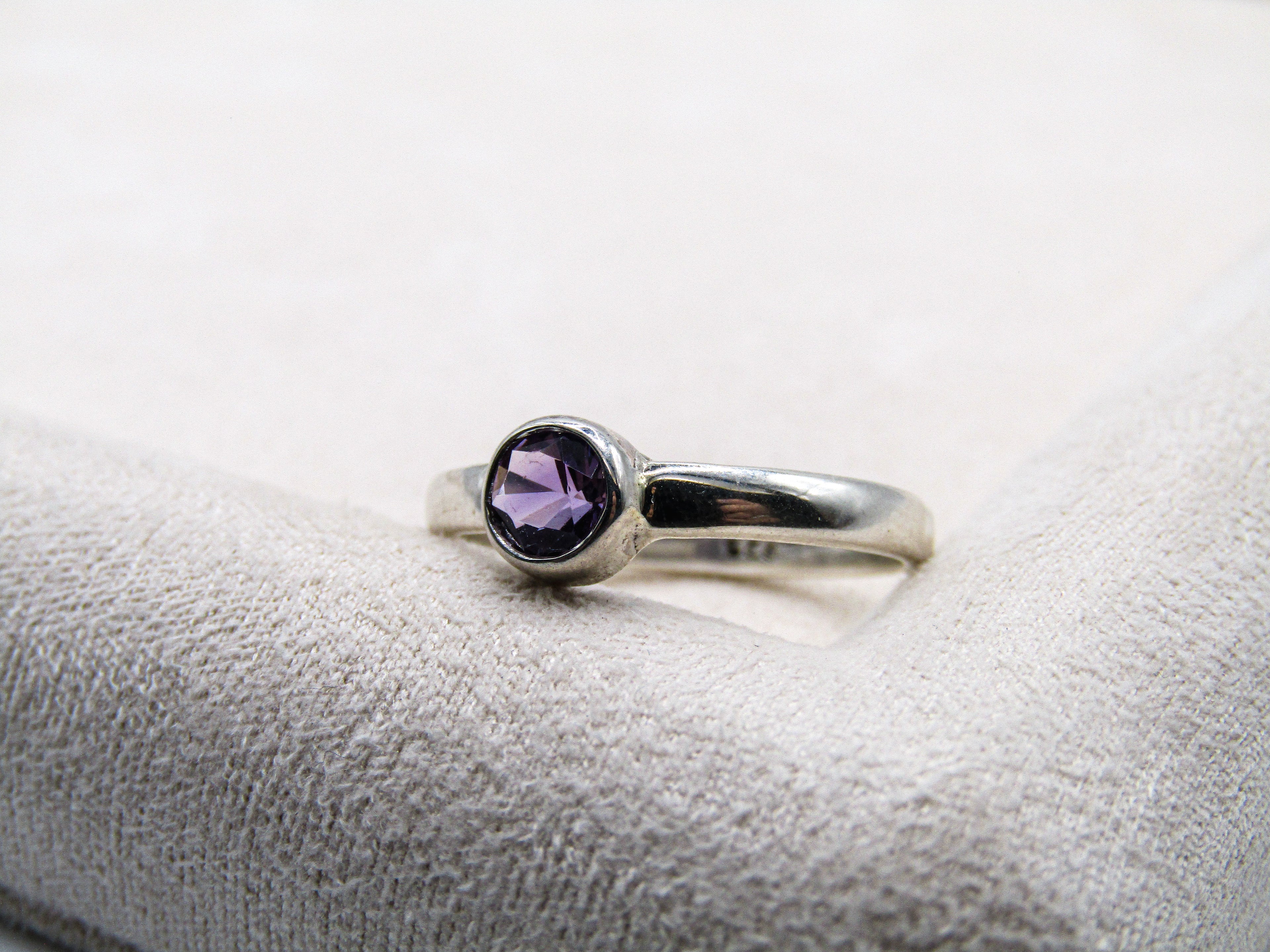 Silver ring with a purple gemstone on a textured white surface