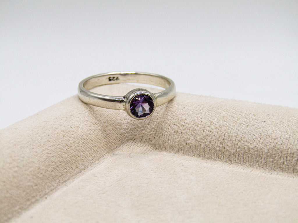 Silver ring with a purple gemstone on a beige cushion
