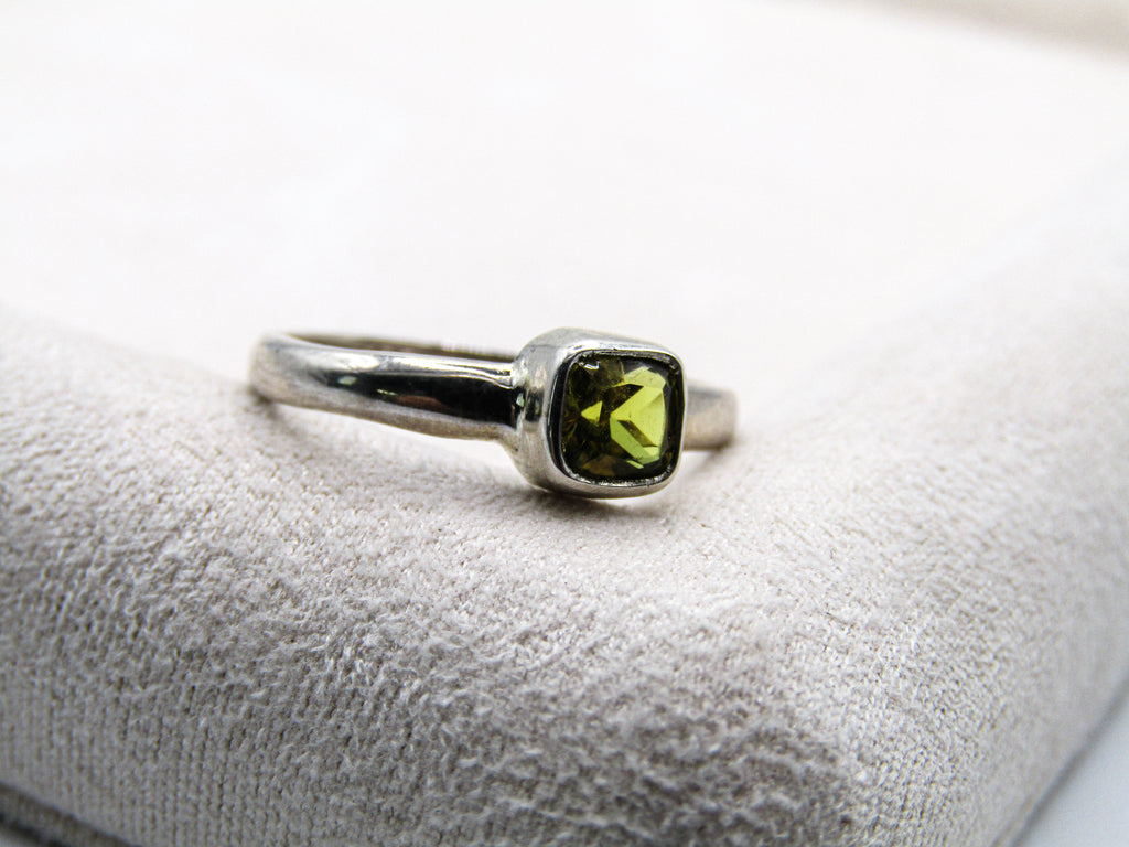 Silver ring with a green gemstone on a white cushion