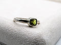Silver ring with a green gemstone on a white cushion