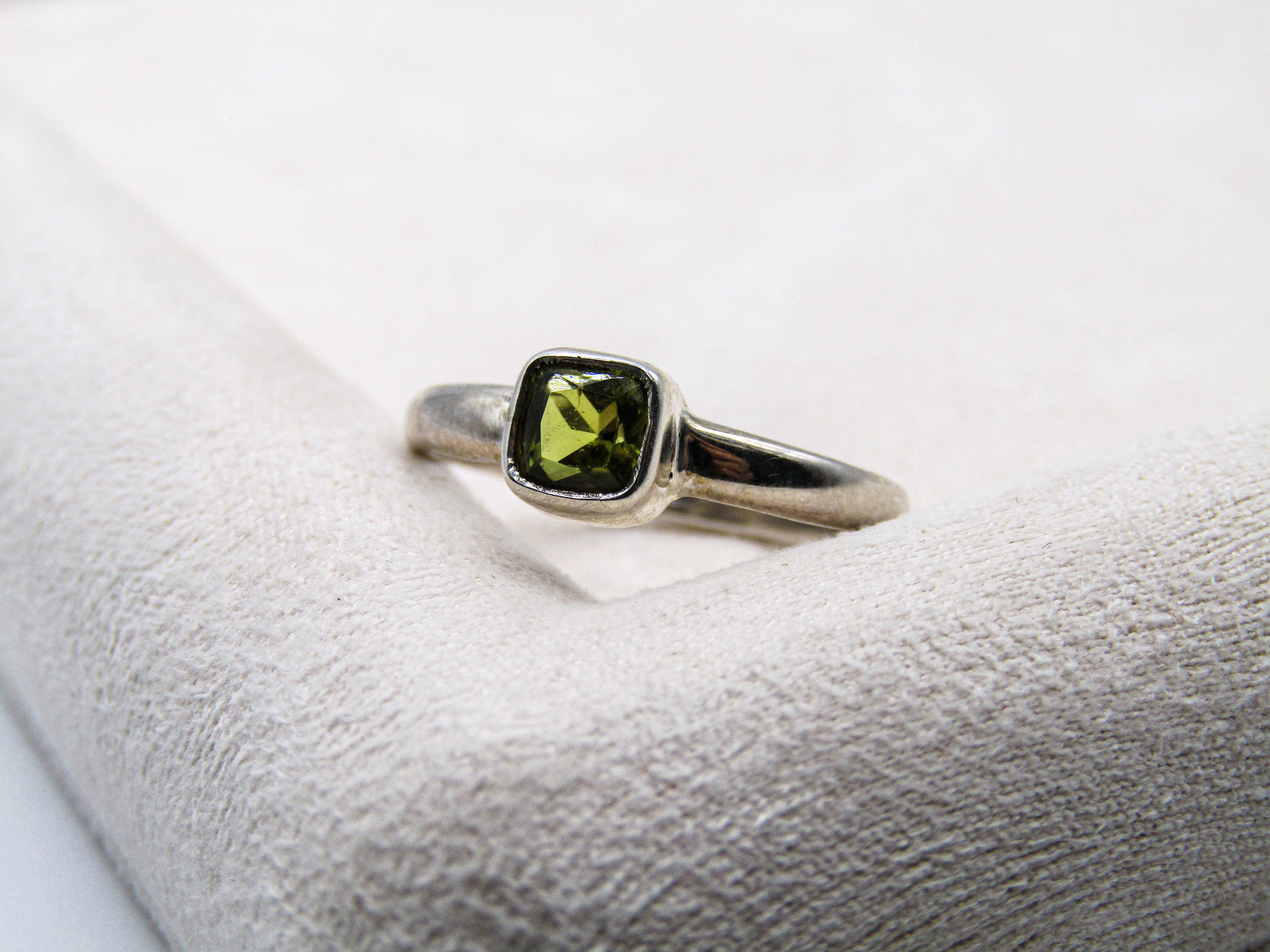 Silver ring with a green gemstone on a white cushion