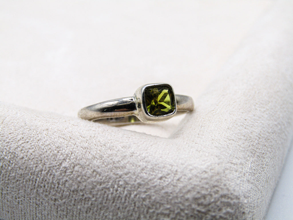 Silver ring with a green gemstone on a white cushion