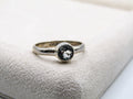 Silver ring with a black gemstone on a textured surface