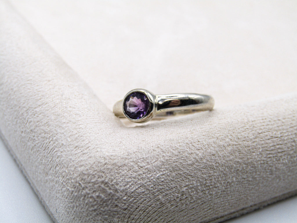 Silver ring with a purple gemstone on a textured white surface