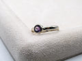 Silver ring with a purple gemstone on a textured white surface