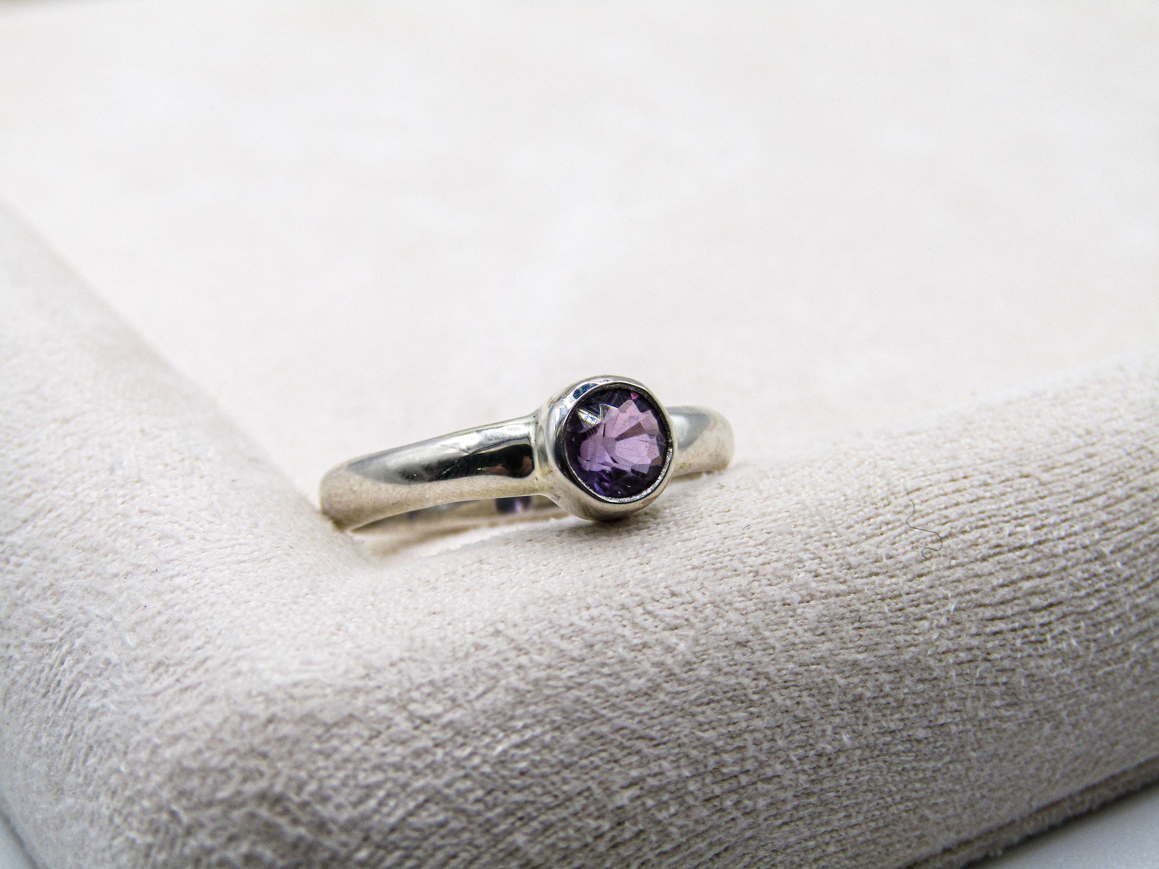 Silver ring with a purple gemstone on a white cushion