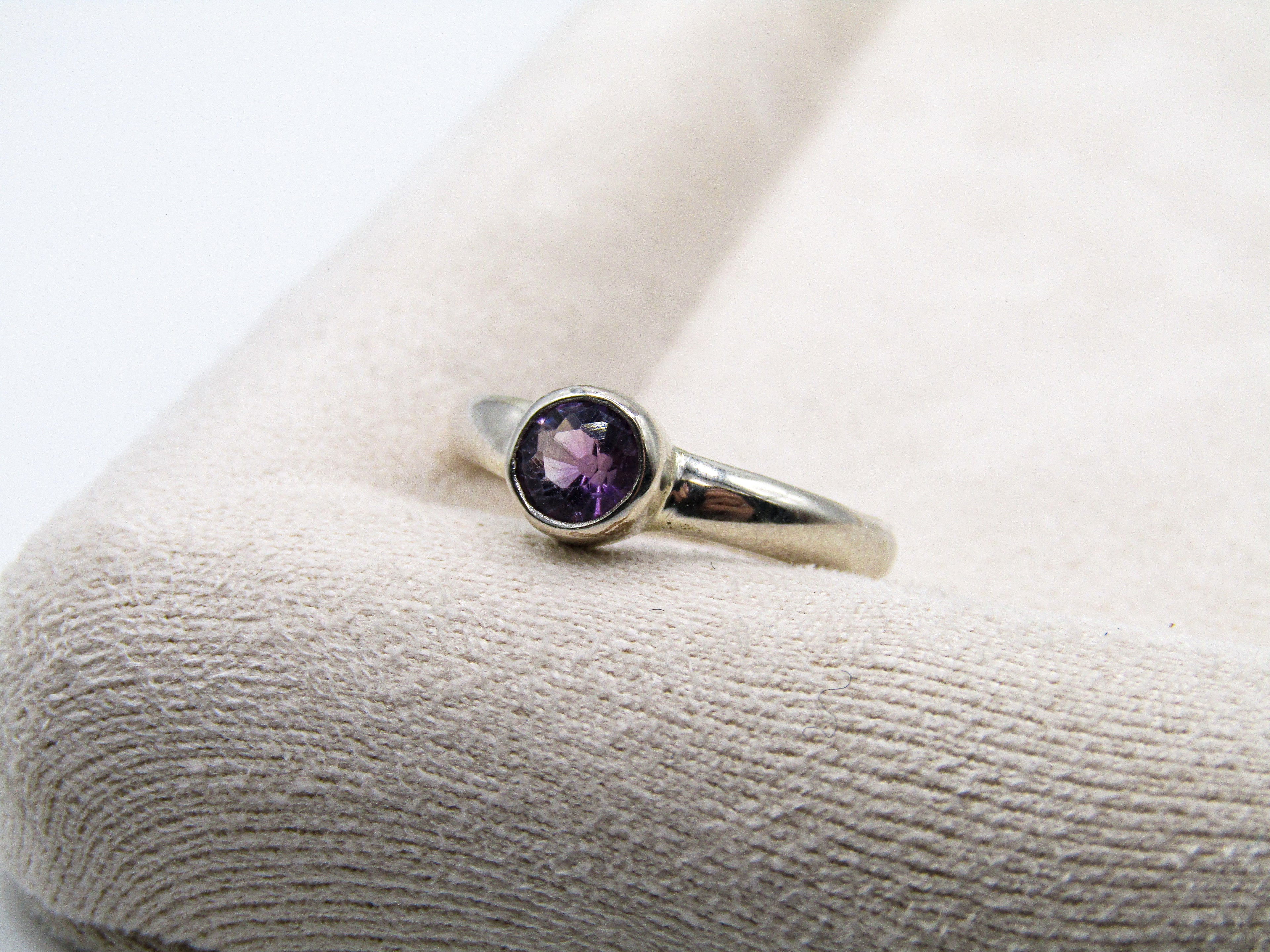 Silver ring with a purple gemstone on a textured white surface