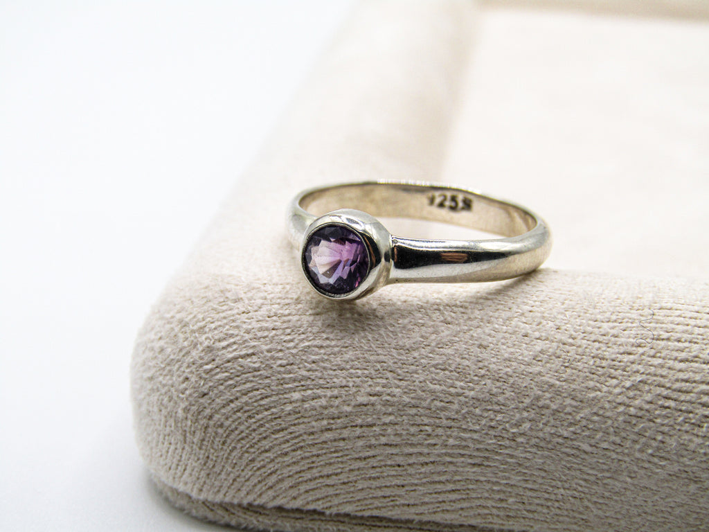 Silver ring with a purple gemstone on a textured surface