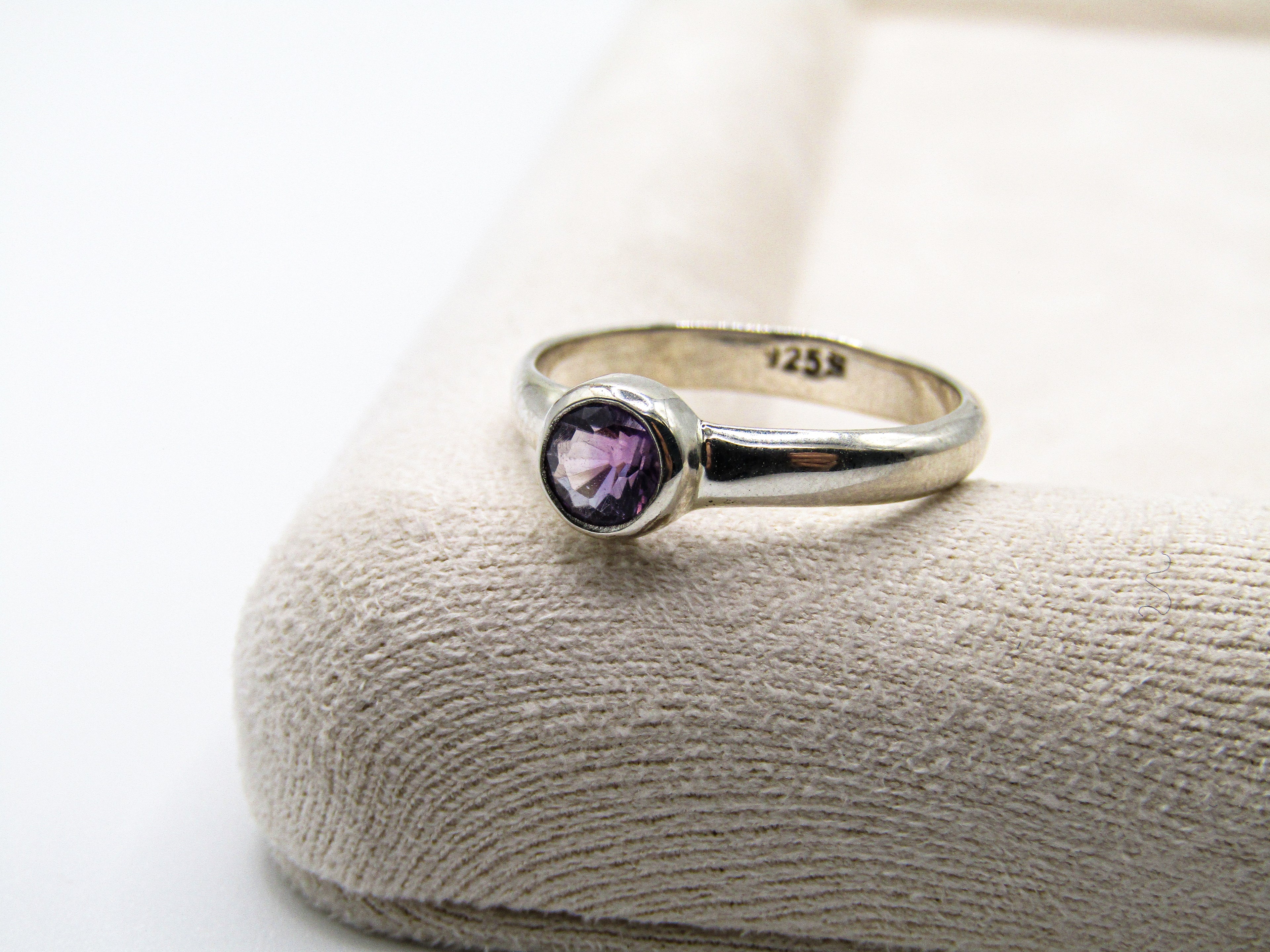 Silver ring with a purple gemstone on a textured surface