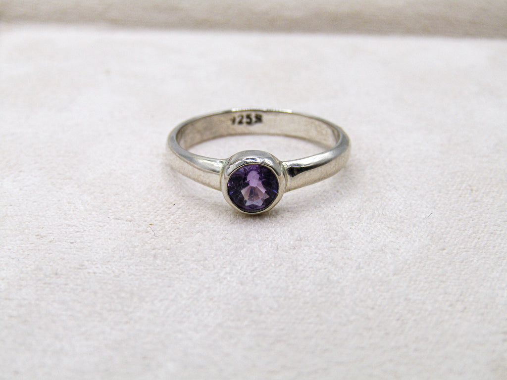 Silver ring with a purple gemstone on a white fabric background
