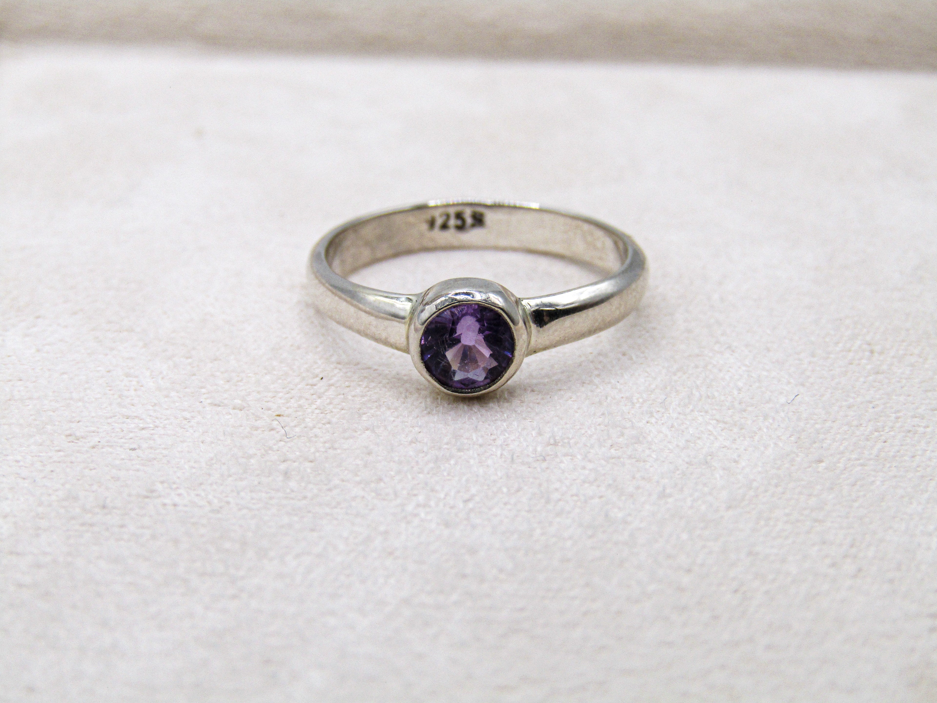 Silver ring with a purple gemstone on a white fabric background